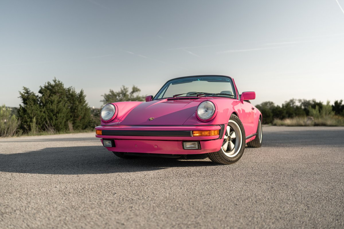 A bright pink Porsche 911 Targa, featuring classic Fuchs rims and black trim, parked outdoors.