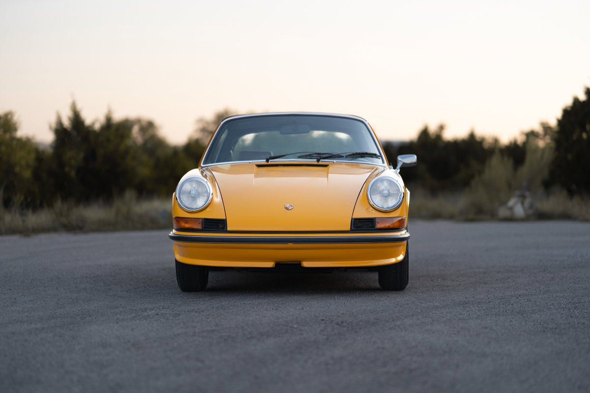 Front view of a yellow 1973 Porsche 911 Targa with chrome trim and Fuchs wheels.