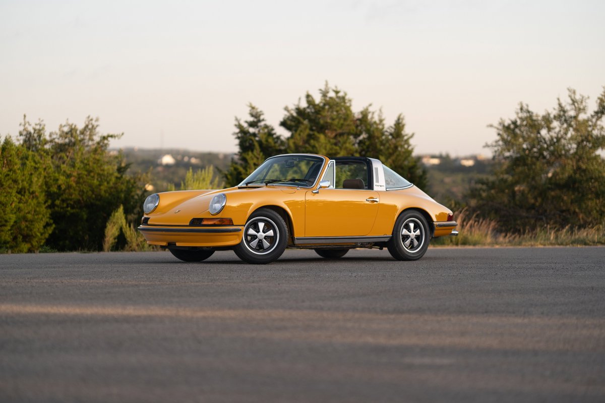 A signal yellow 1973 Porsche 911S Targa with chrome trim and five-spoke rims on a paved road.