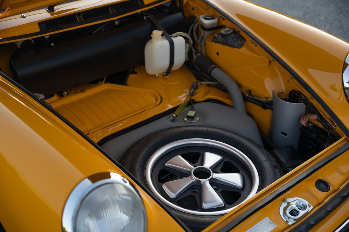 Front trunk of a Signal Yellow 1973 Porsche 911S Targa, showing spare tire and silver alloy rims.