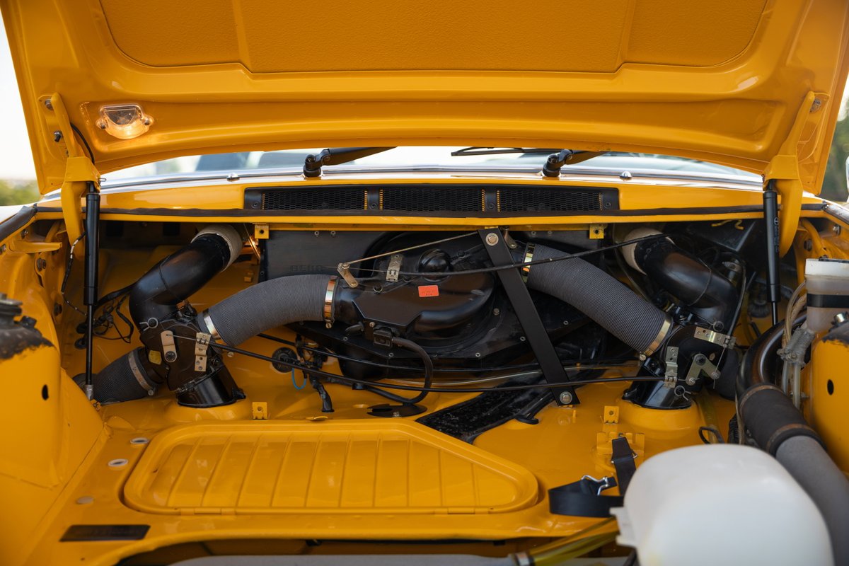 Yellow 1973 Porsche 911S Targa engine bay with twin turbo intake piping.
