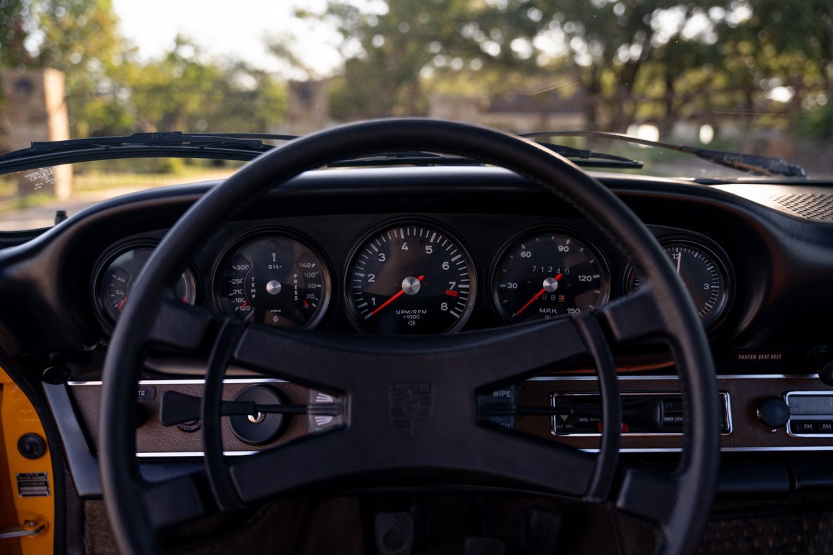 1973 Porsche 911S Targa dashboard in signal yellow. Features classic gauges, a black steering wheel, and wood-grain trim.