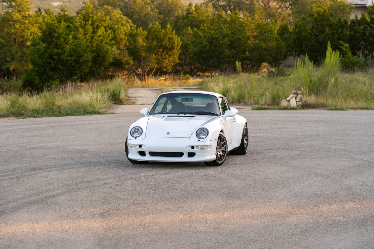 White 1997 Porsche 993 C4S coupe with grey multi-spoke rims parked on asphalt.