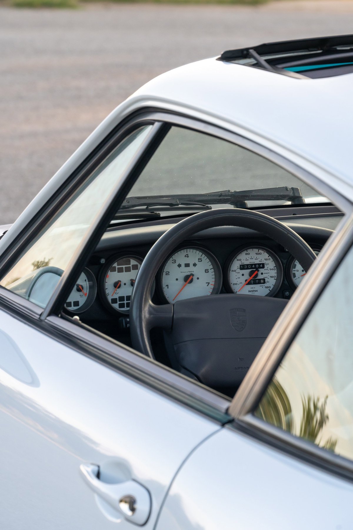 Interior view of a 1997 Porsche 993 C4S in Glacier White, showing the dashboard gauges and steering wheel.