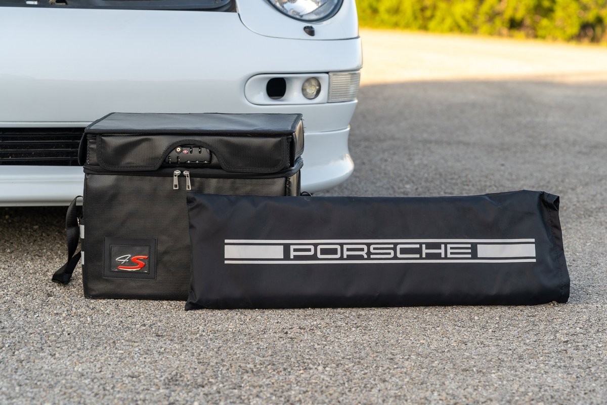Black Porsche tool bags with silver accents and the Porsche script logo sit beside a white 1997 Porsche 993 C4S.