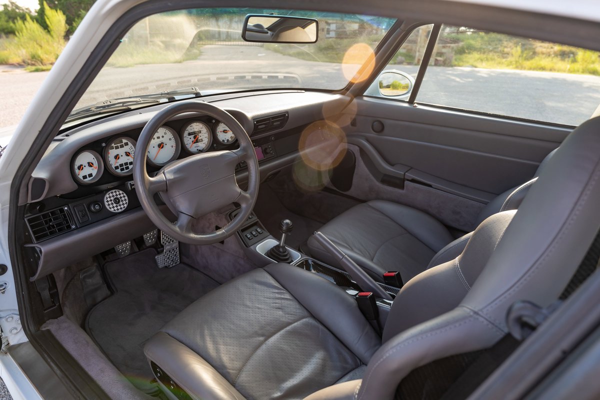 Interior of a Glacier White 1997 Porsche 993 C4S showing gray leather seats and the instrument cluster.