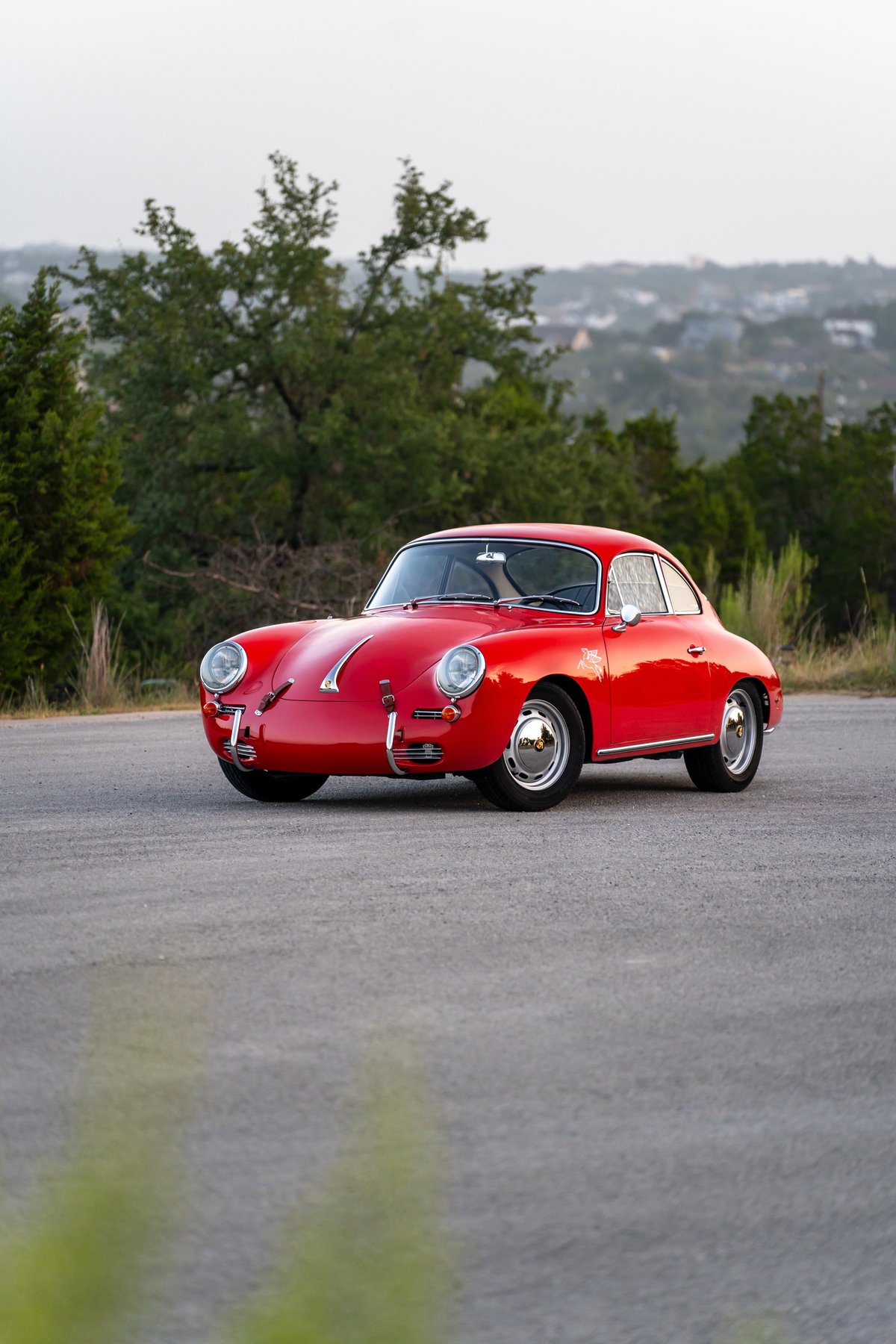A vintage, signal red 1965 Porsche 356C coupe with chrome rims sits on asphalt.