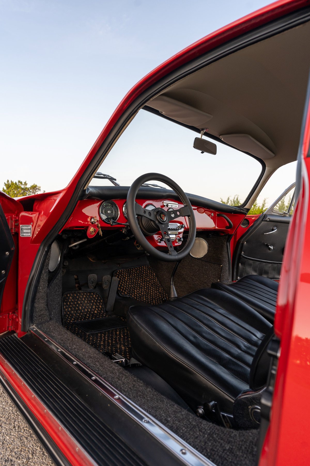 Red 1965 Porsche 356C interior with black leather seats, vintage steering wheel, and patterned floor mats.