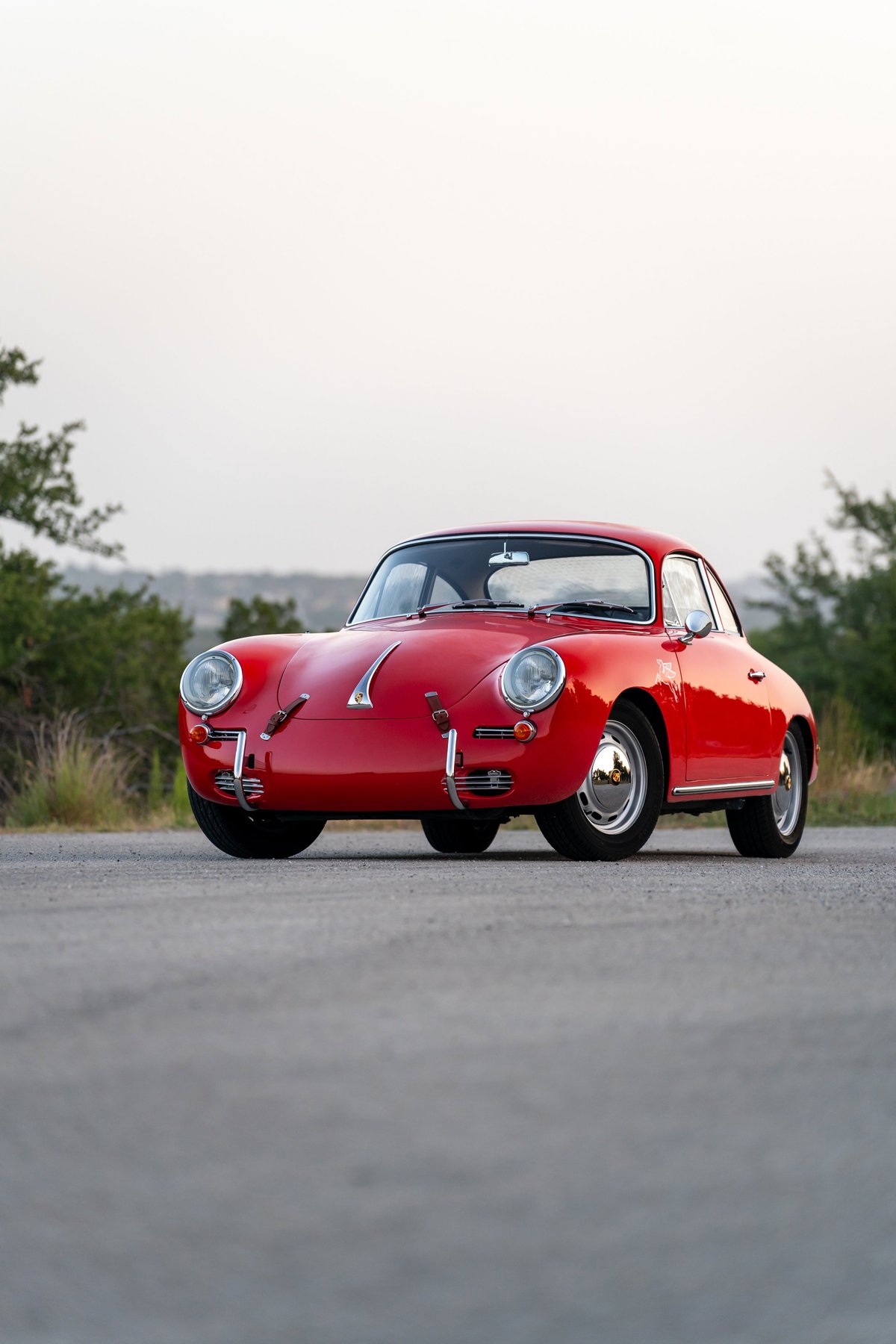 A signal red 1965 Porsche 356C coupe with chrome hubcaps on a paved road.