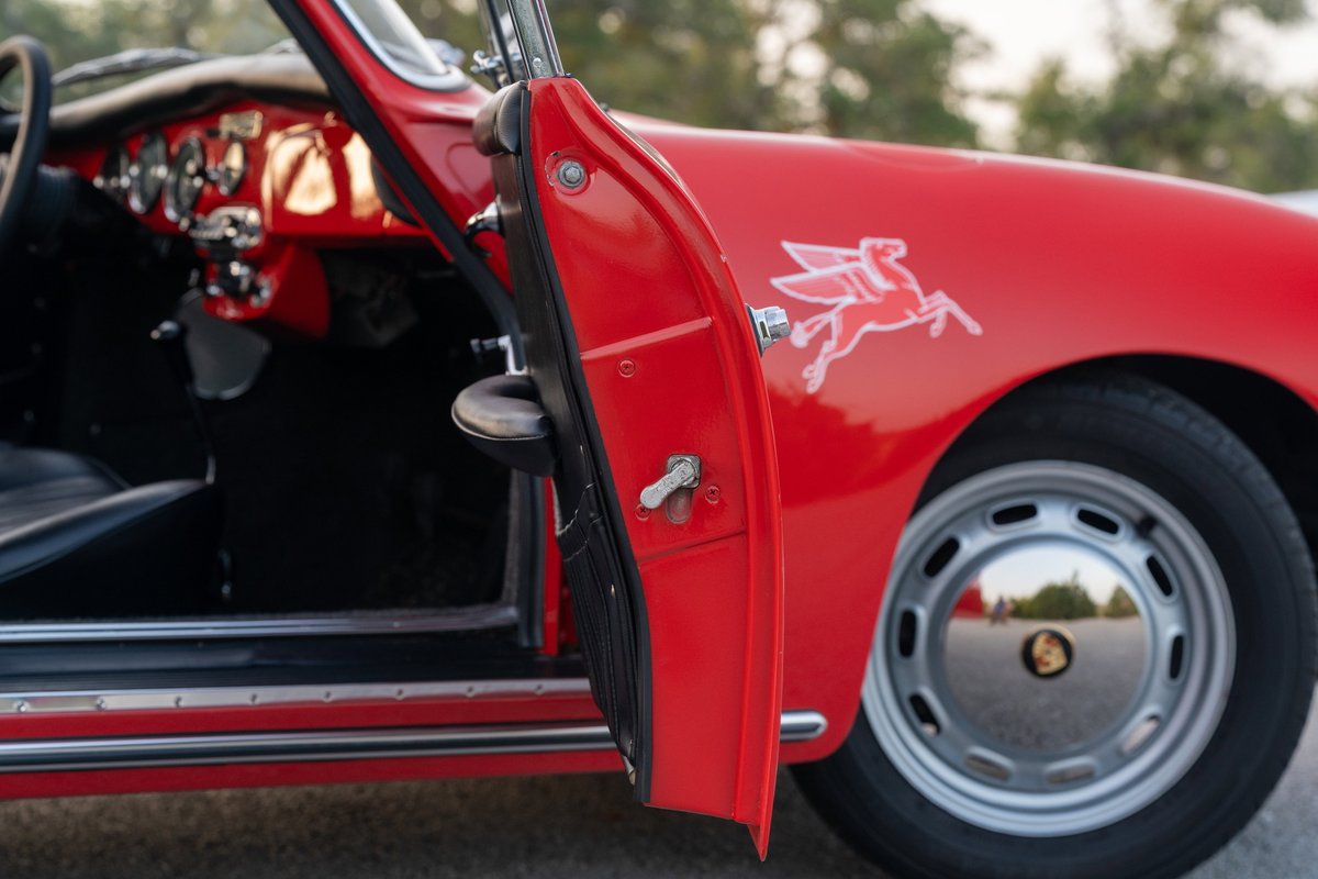 Red 1965 Porsche 356C with flying horse livery, chrome hubcap rims, and open door.