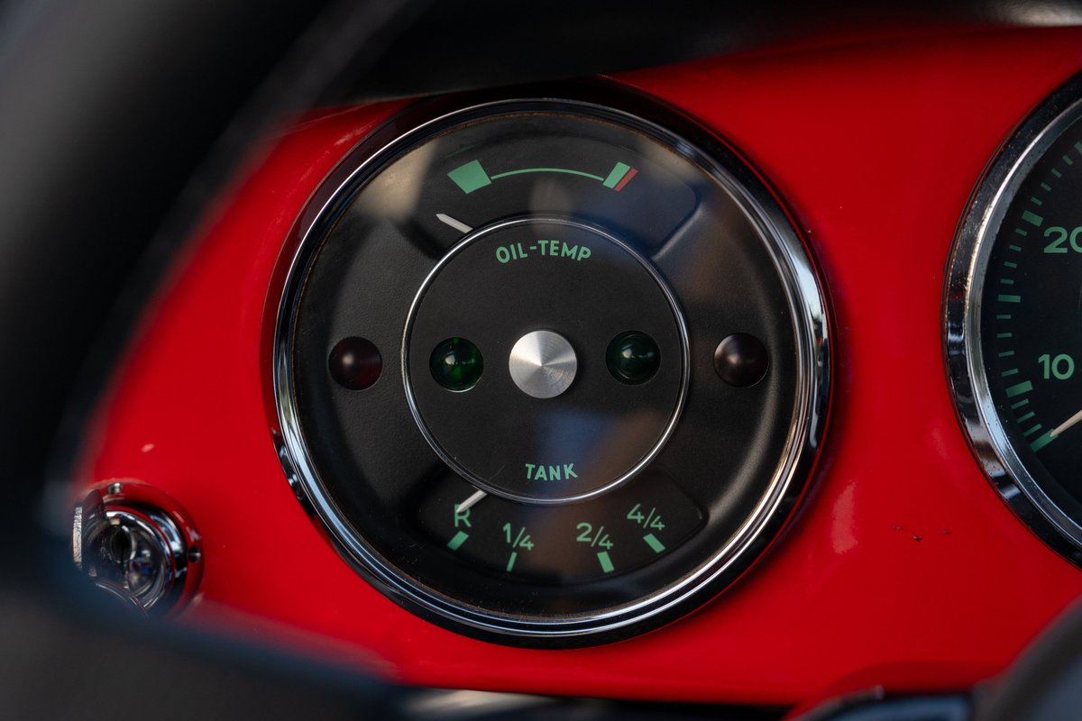 Close-up of a vintage Porsche 356C dashboard in Signal Red, showing the oil temp and fuel gauges.