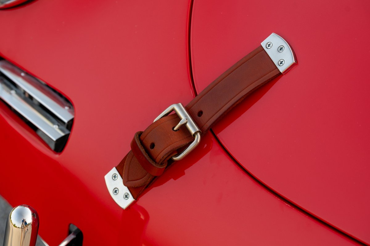 1965 Porsche 356C in Signal Red with a brown leather hood strap and chrome trim.