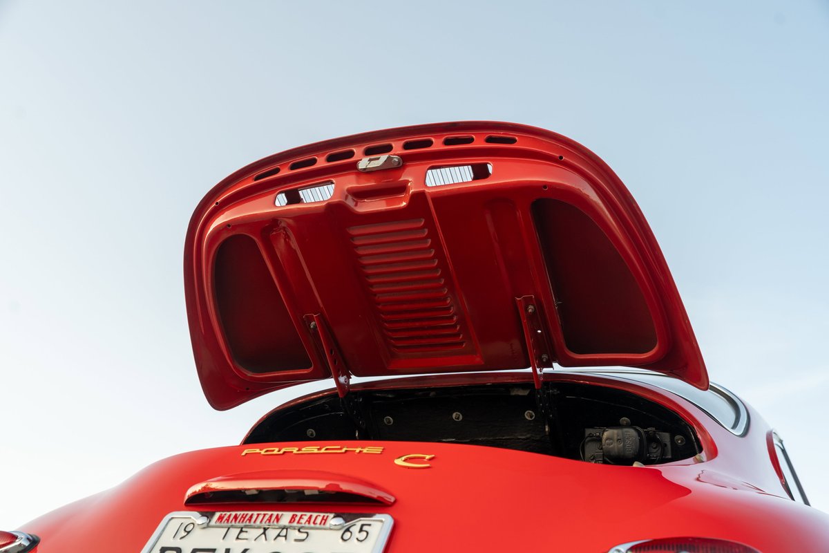 Rear view of a signal red 1965 Porsche 356C with the trunk open, showing interior details and the engine compartment.