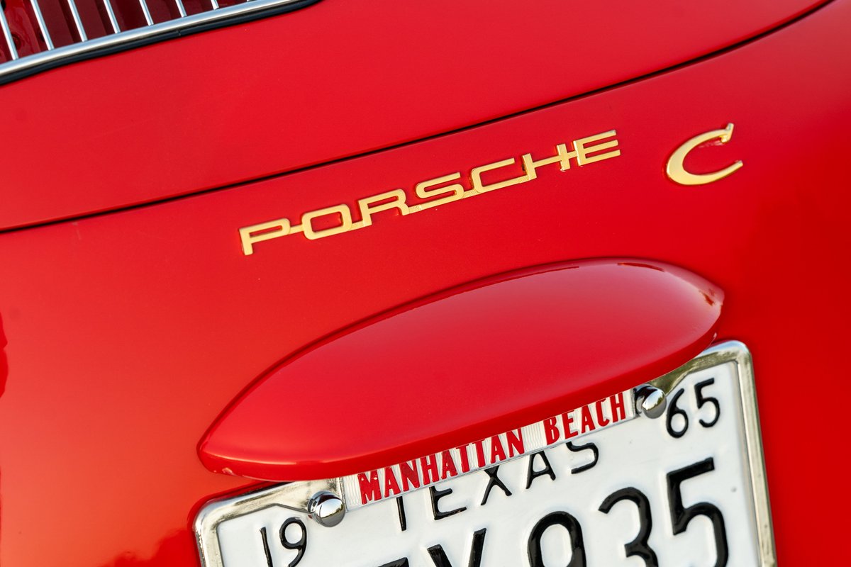 Golden "Porsche C" emblem on a Signal Red 1965 Porsche 356C with a Texas license plate.