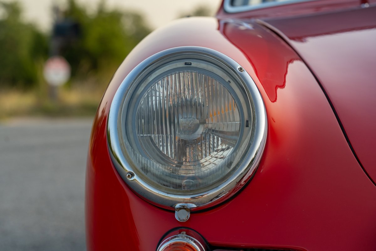 Close-up of a 1965 Porsche 356C headlight, Signal Red paint, chrome trim, detailed lens.