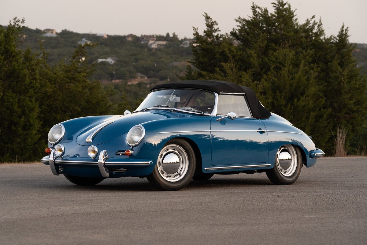 A blue 1960 Porsche 356B Roadster with chrome hubcaps and a black convertible top sits on asphalt.