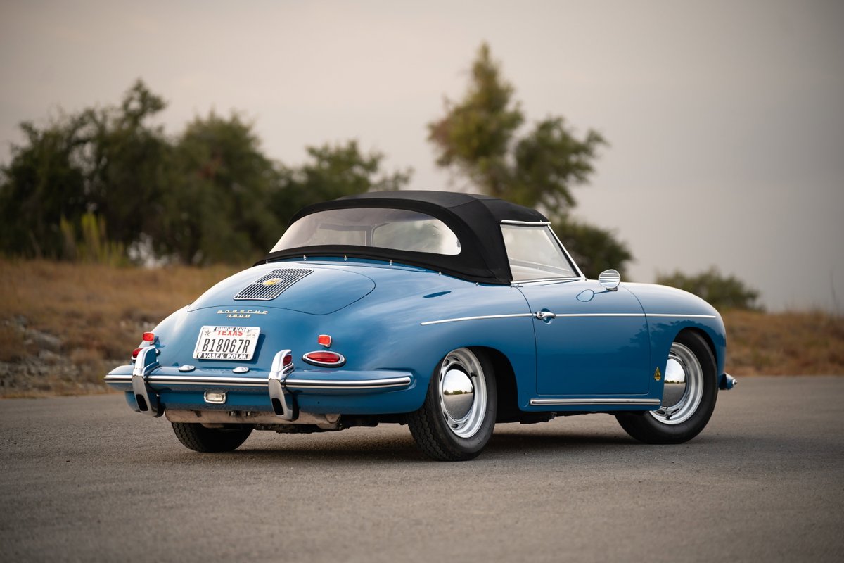Rear 3/4 view of a royal blue 1960 Porsche 356B Roadster with a black soft top and chrome rims.