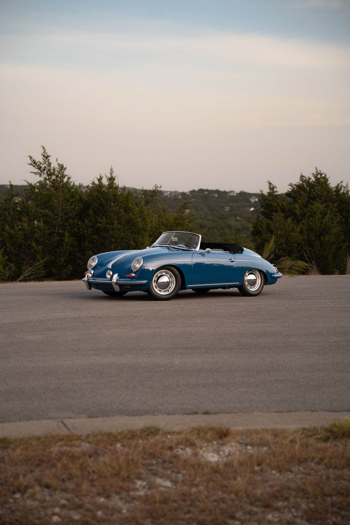 A royal blue 1960 Porsche 356B Roadster with chrome rims parked on asphalt.