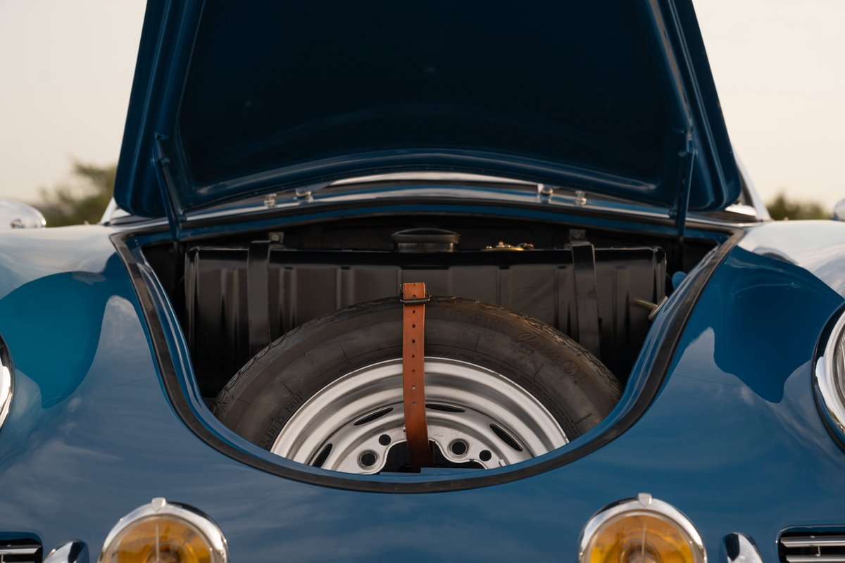 Blue 1960 Porsche 356B Roadster front trunk with spare tire and chrome rims.