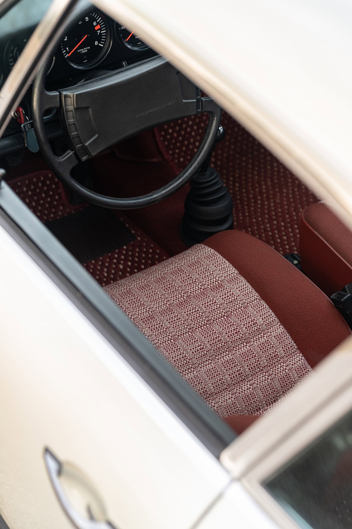 1974 Porsche 911 coupe interior with patterned red fabric seats and dashboard.