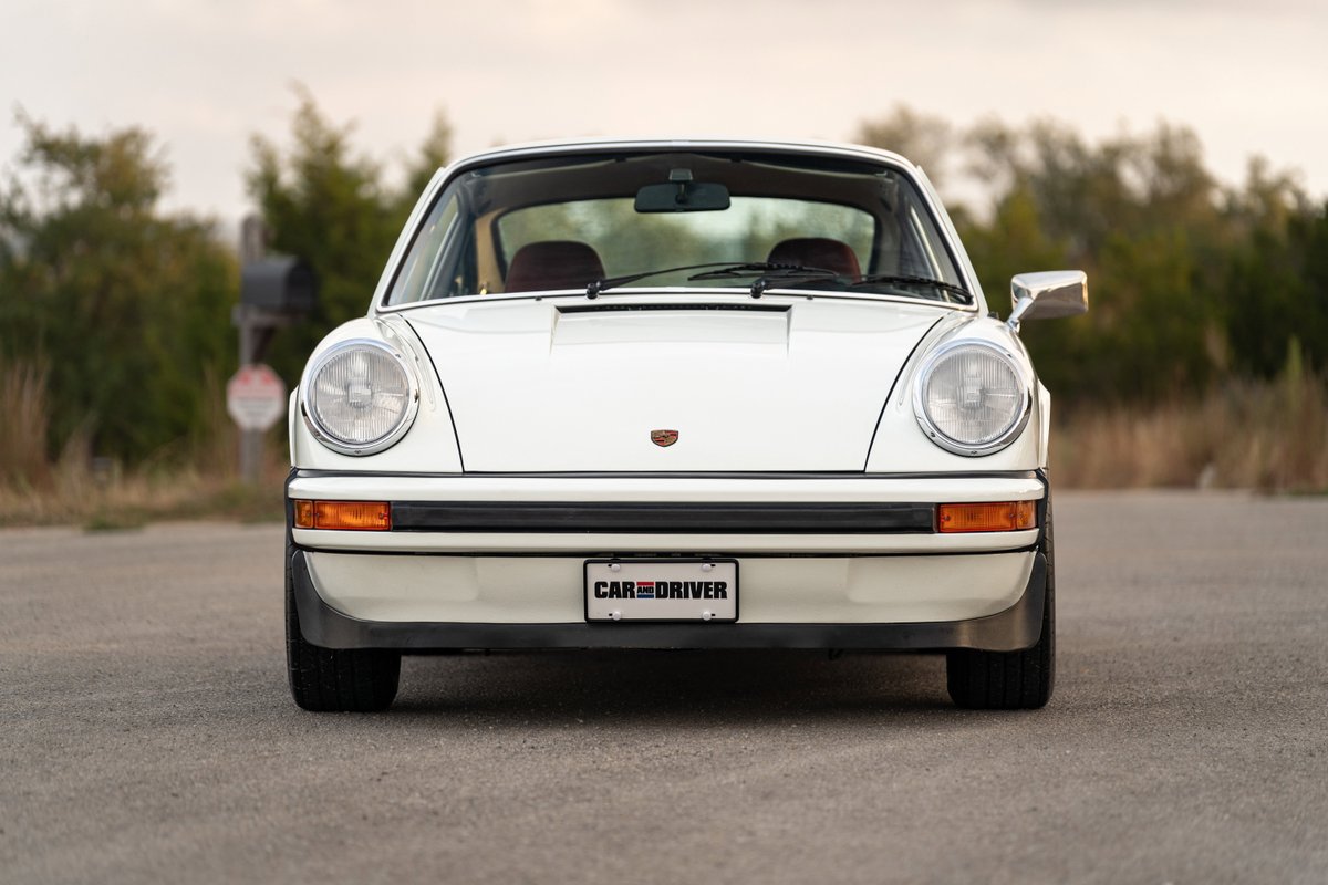 Front view of a white 1974 Porsche 911 coupe with black trim and a "Car and Driver" license plate.