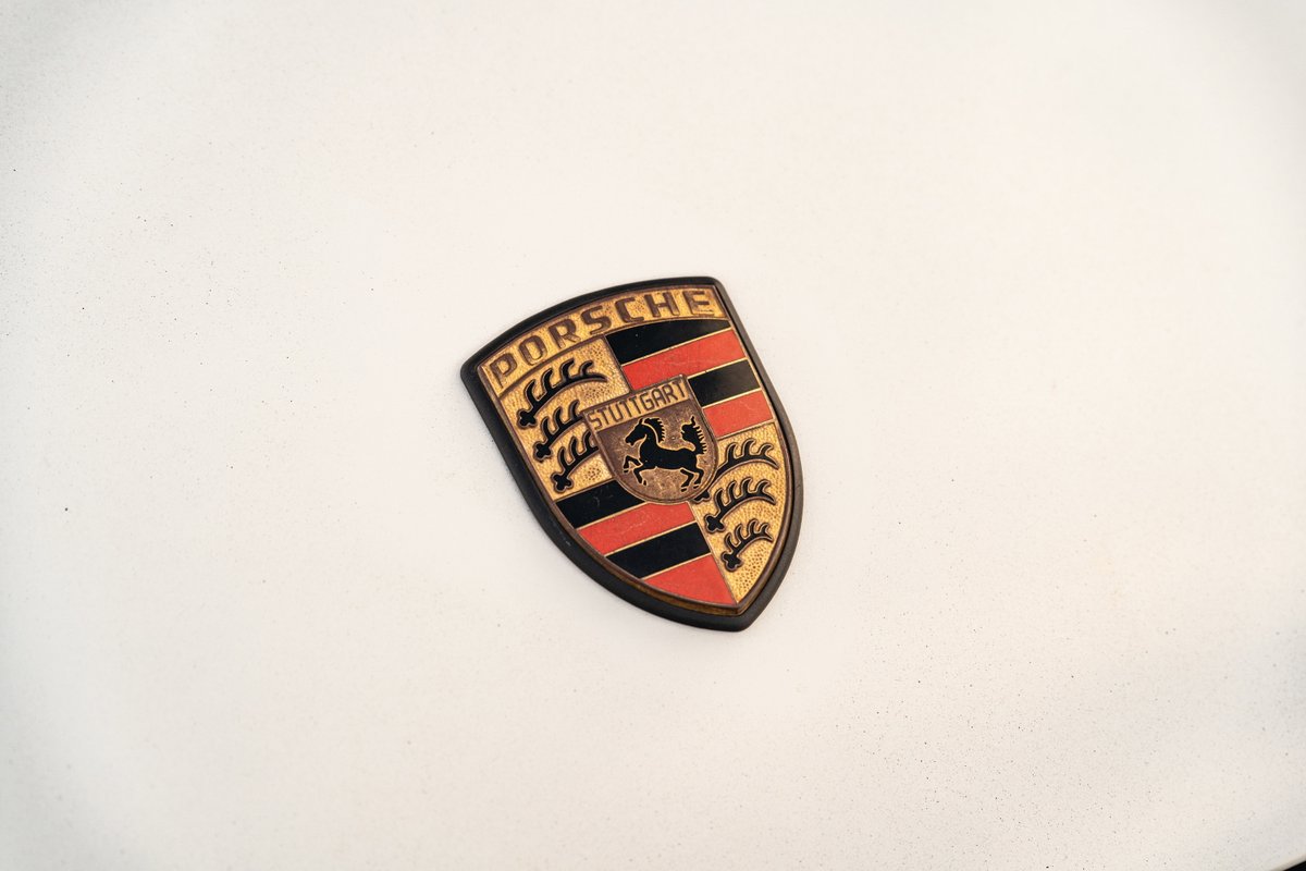 Close up of a vintage Porsche crest badge on a white 1974 Porsche 911 Coupe.