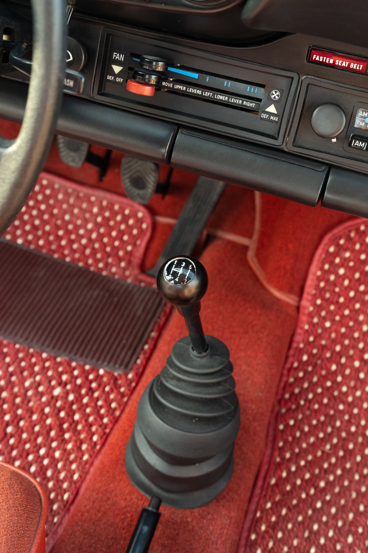 Interior shot of a 1974 Porsche 911 Coupe with red carpet and manual shifter.