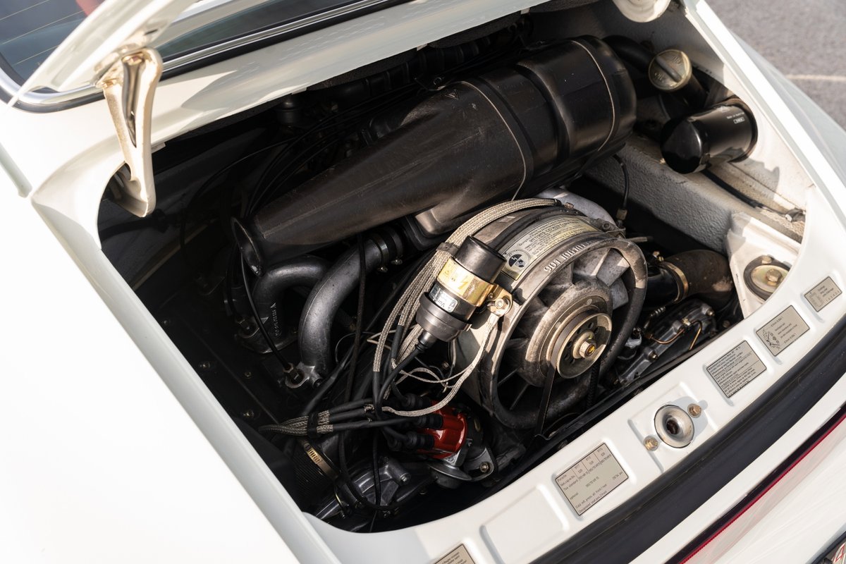 White 1974 Porsche 911 coupe engine bay, flat-six air-cooled engine, black airbox and intake plumbing.