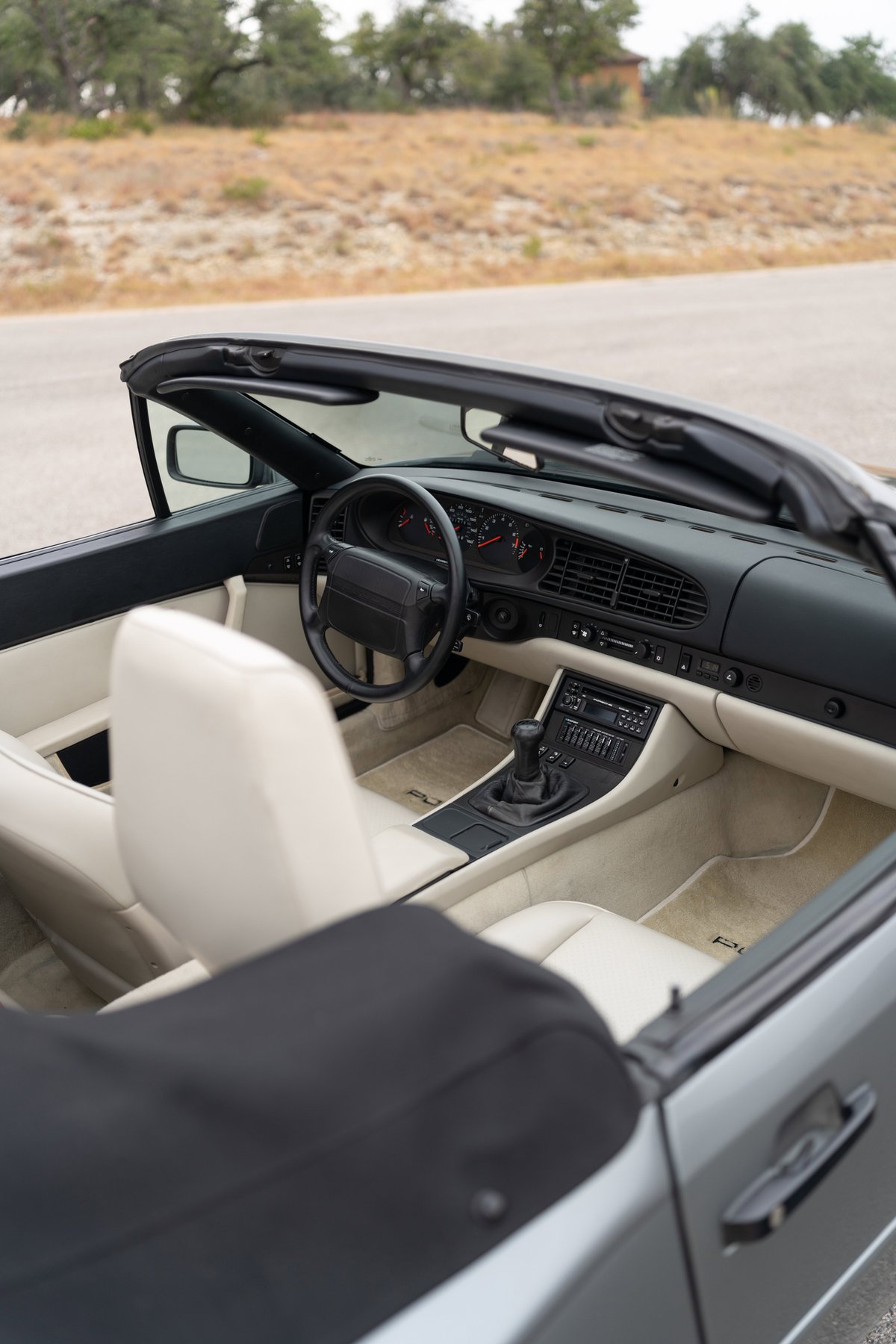 Interior view of a 1990 Porsche 944 S2 Cabriolet in Titanium Metallic with light beige leather seats and black soft-top.