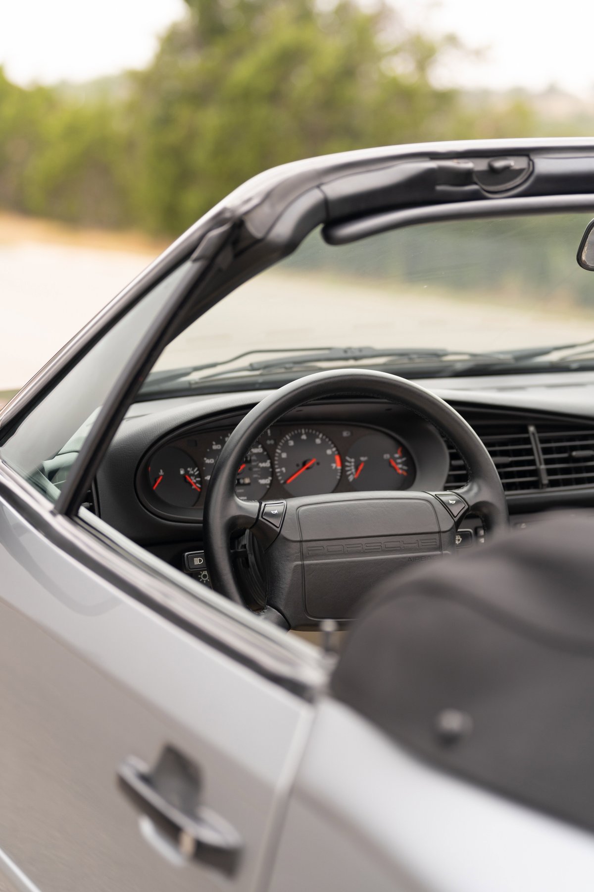 Close-up interior of a silver 1990 Porsche 944 S2 Cabriolet, showing the steering wheel and dashboard.