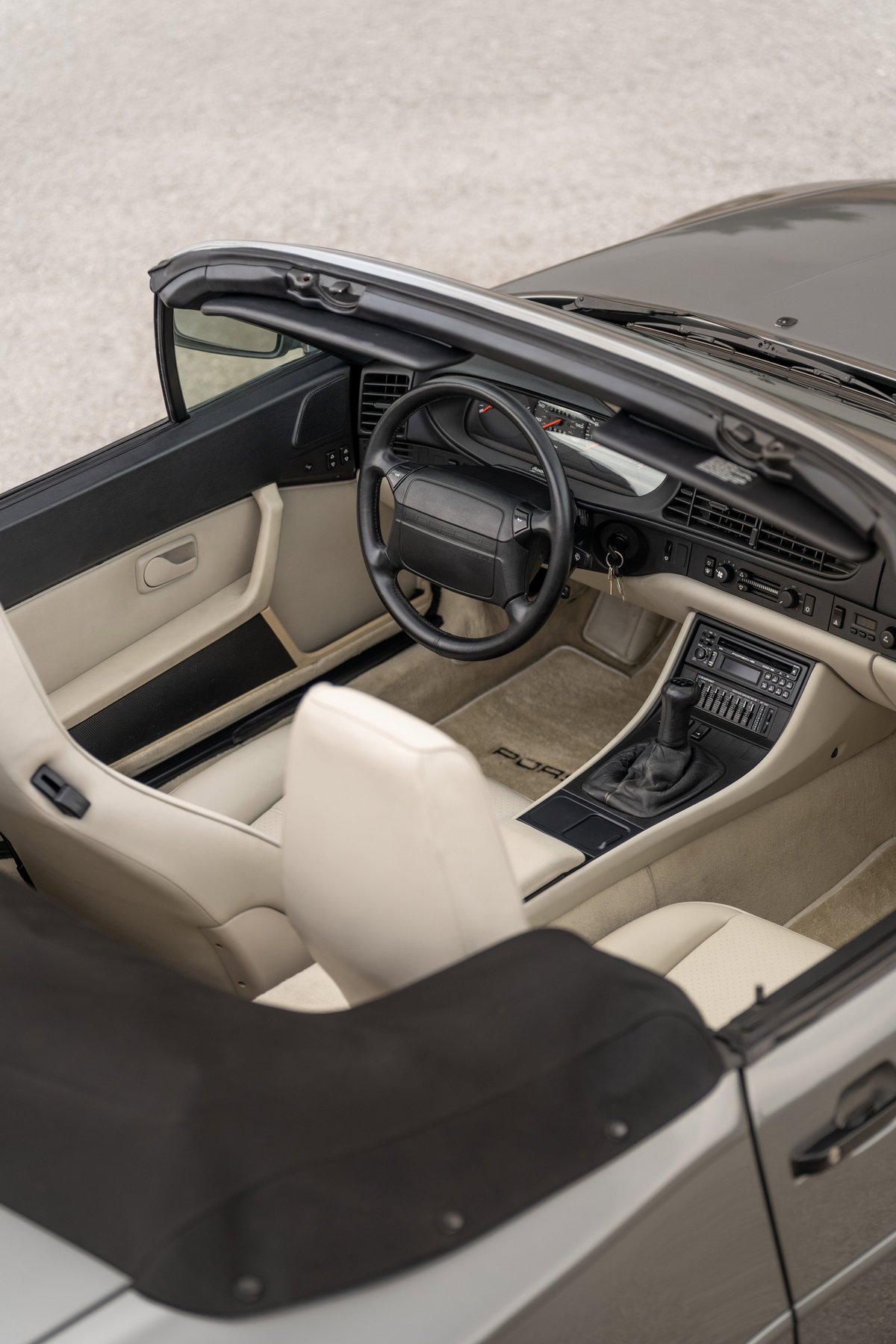 Interior view of a 1990 Porsche 944 S2 Cabriolet in Titanium Metallic, featuring cream leather seats and dashboard trim.
