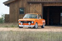 Orange 1976 BMW 2002 with vintage rally lights and silver multi-spoke rims.