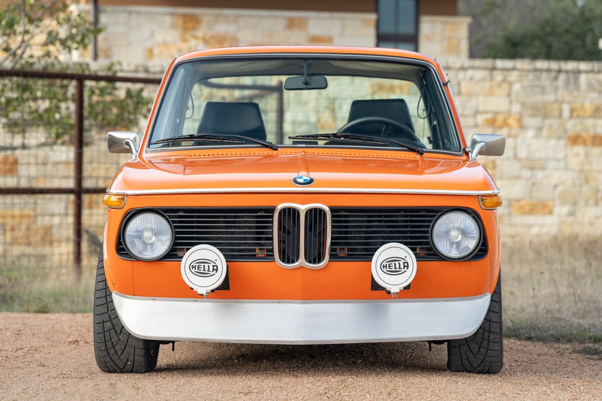 Front view of an Inka Orange 1976 BMW 2002 with Hella fog lights and chrome bumper trim.