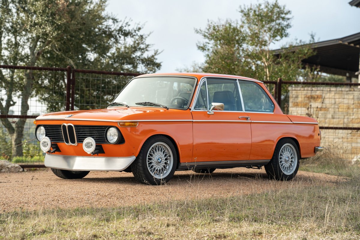 Orange 1976 BMW 2002 with chrome trim and aftermarket alloy rims.