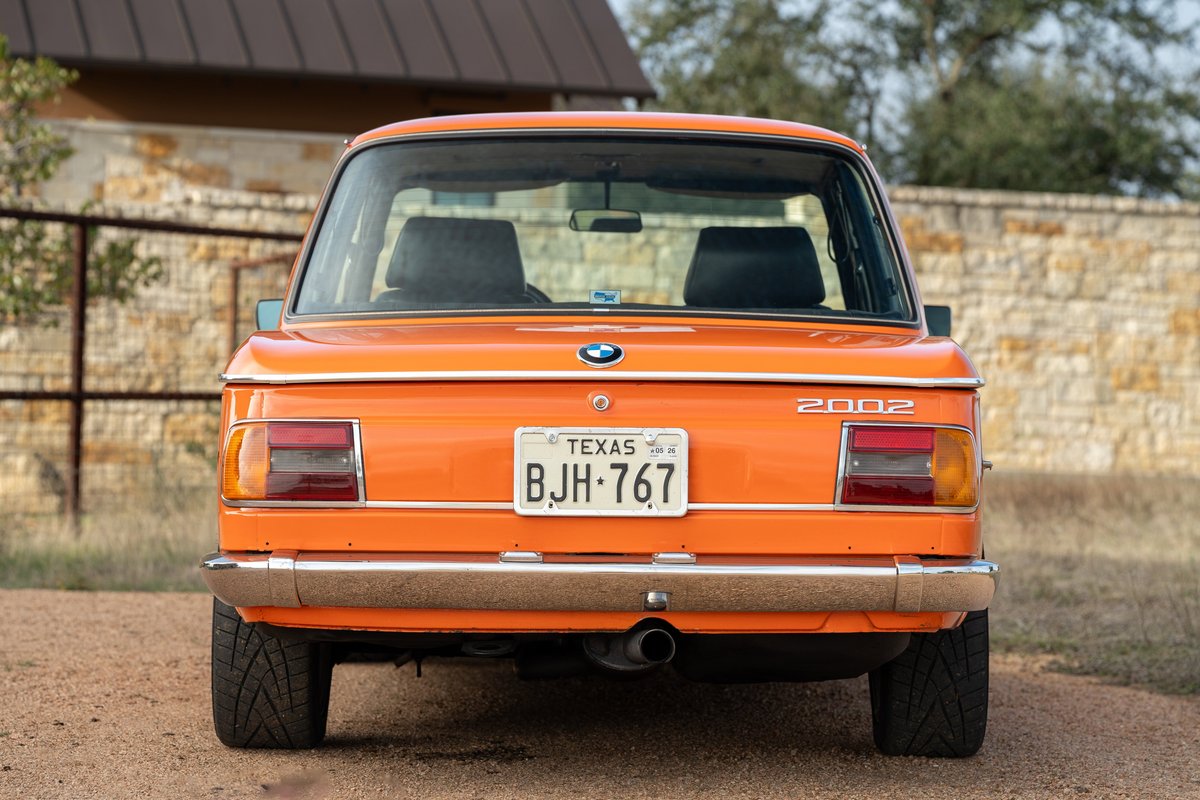 Rear view of an Inka Orange 1976 BMW 2002 with chrome trim and classic rims.