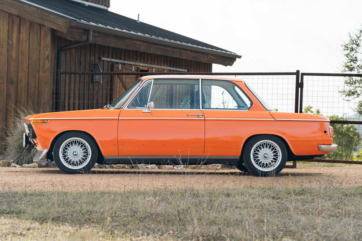 Orange 1976 BMW 2002 two-door coupe with chrome trim and basketweave rims.