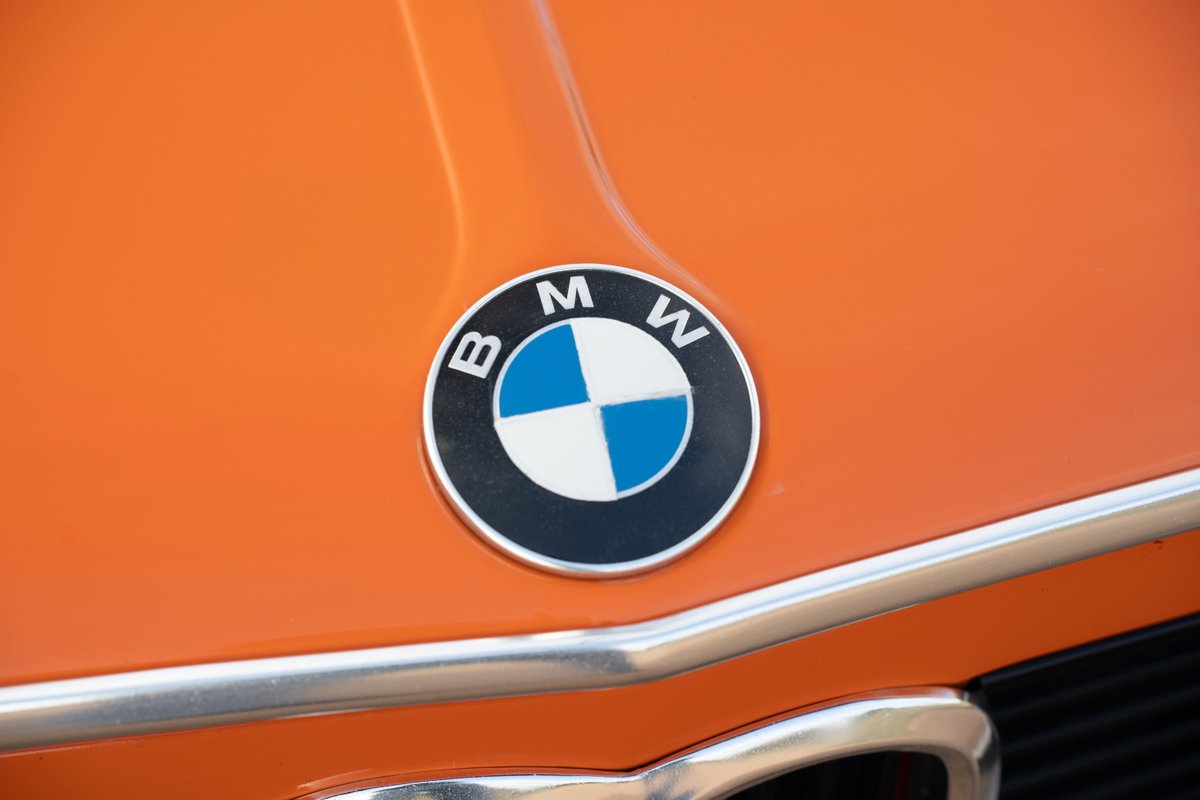 Close up of the BMW emblem on the hood of an Inka Orange 1976 BMW 2002.