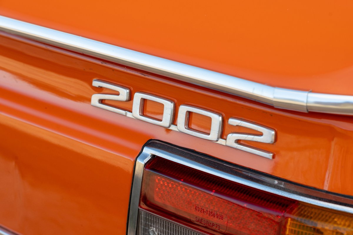 Close-up of an orange 1976 BMW 2002 badge on the trunk lid.