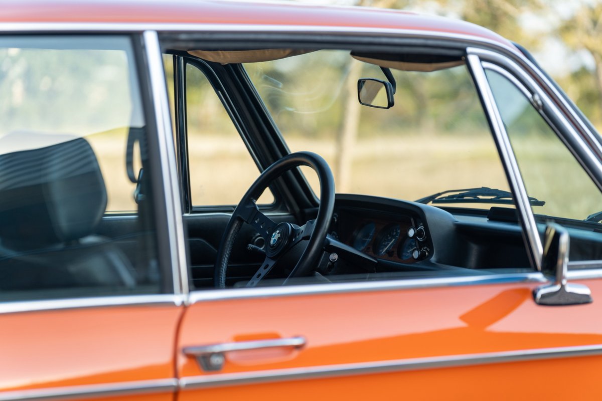 Interior of an orange 1976 BMW 2002, showing the dashboard, steering wheel, and seat.