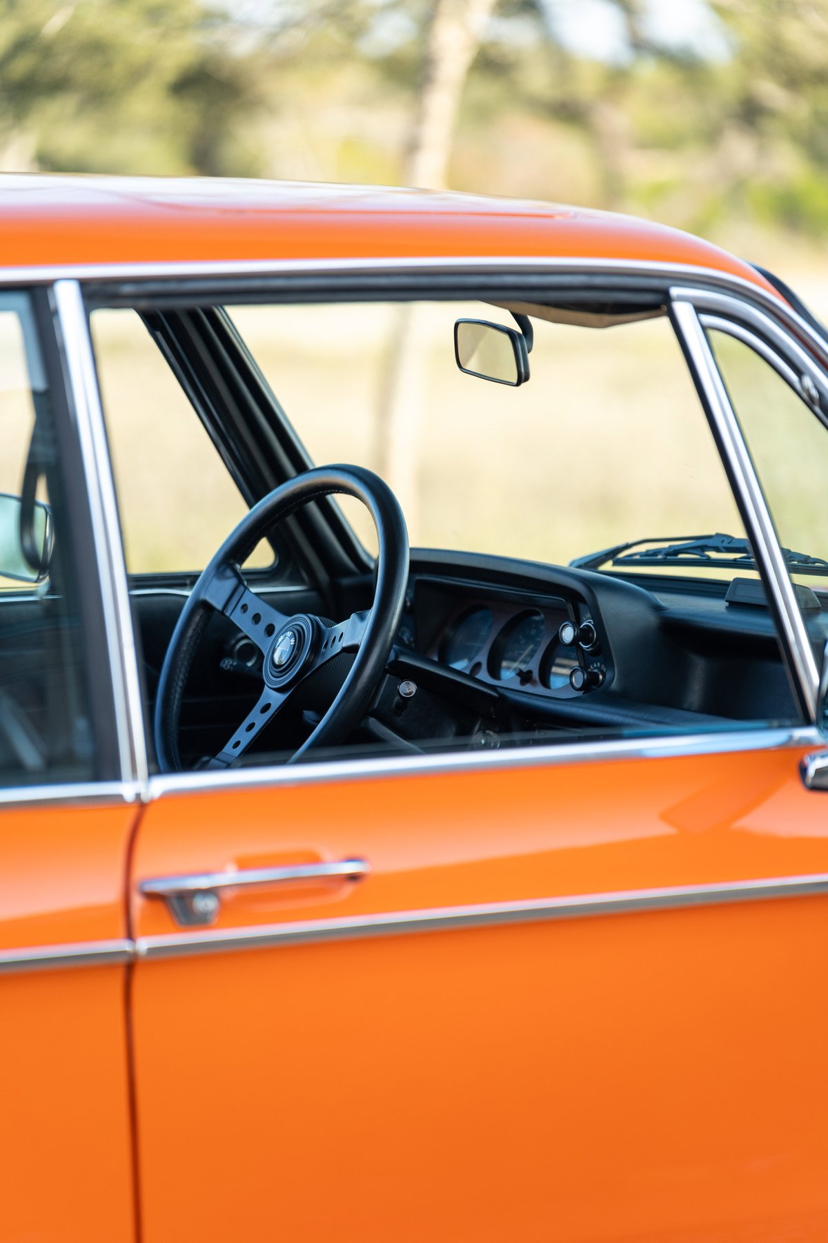 Close up of the interior of an orange 1976 BMW 2002 showing the steering wheel.