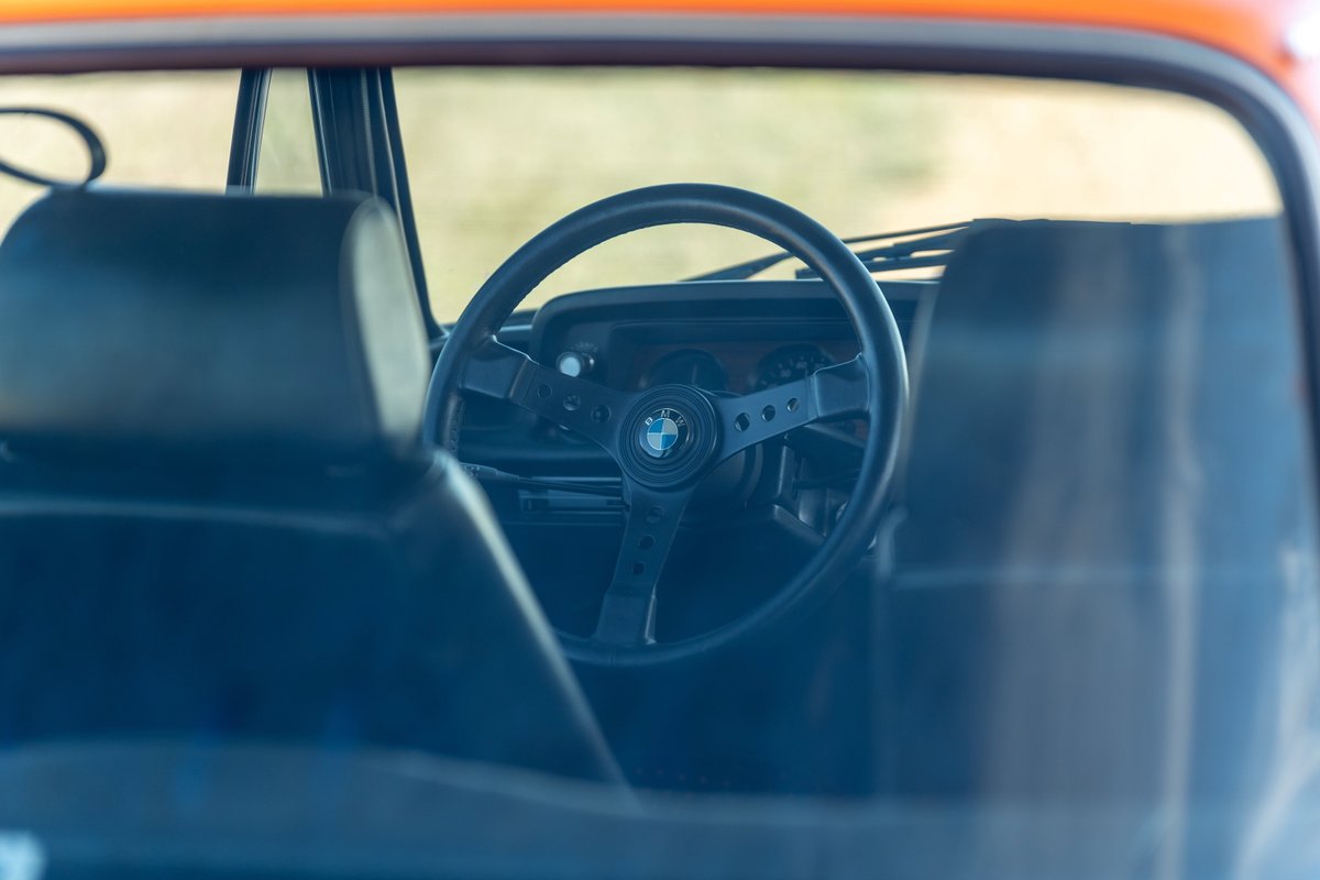 Interior of an Inka Orange 1976 BMW 2002, showing the classic steering wheel and dashboard.