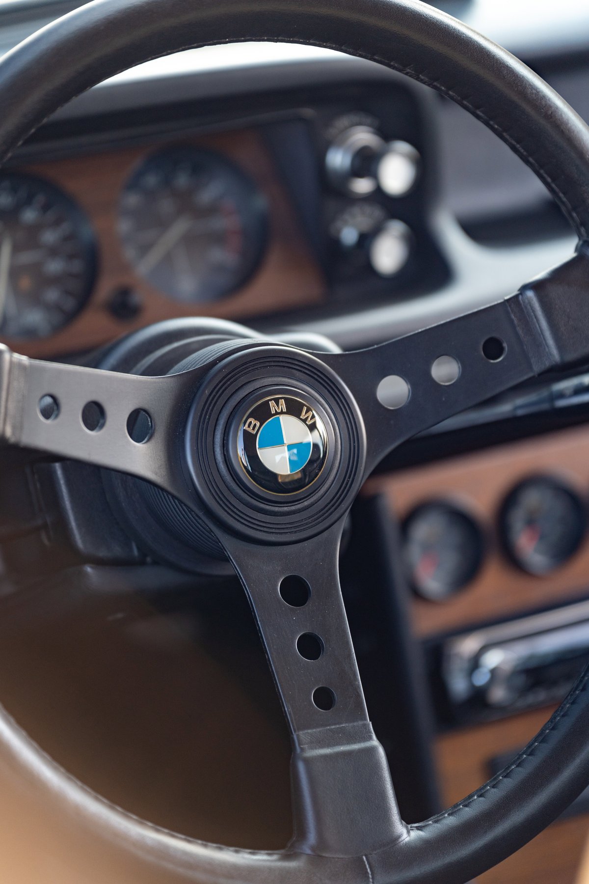 Close-up of a vintage BMW steering wheel with wood trim interior and classic gauges.
