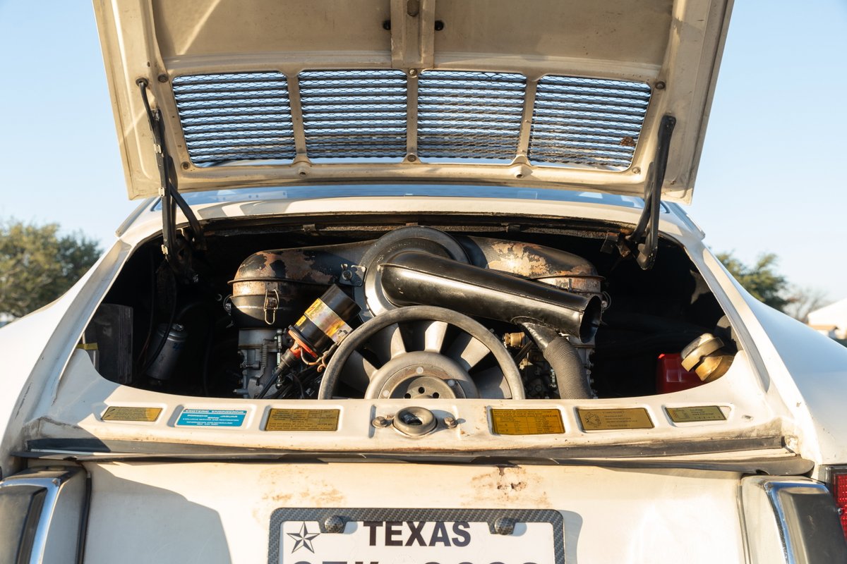 Rear view of a vintage light ivory 1970 Porsche 911T Coupe with its engine compartment open, revealing the flat-six engine.