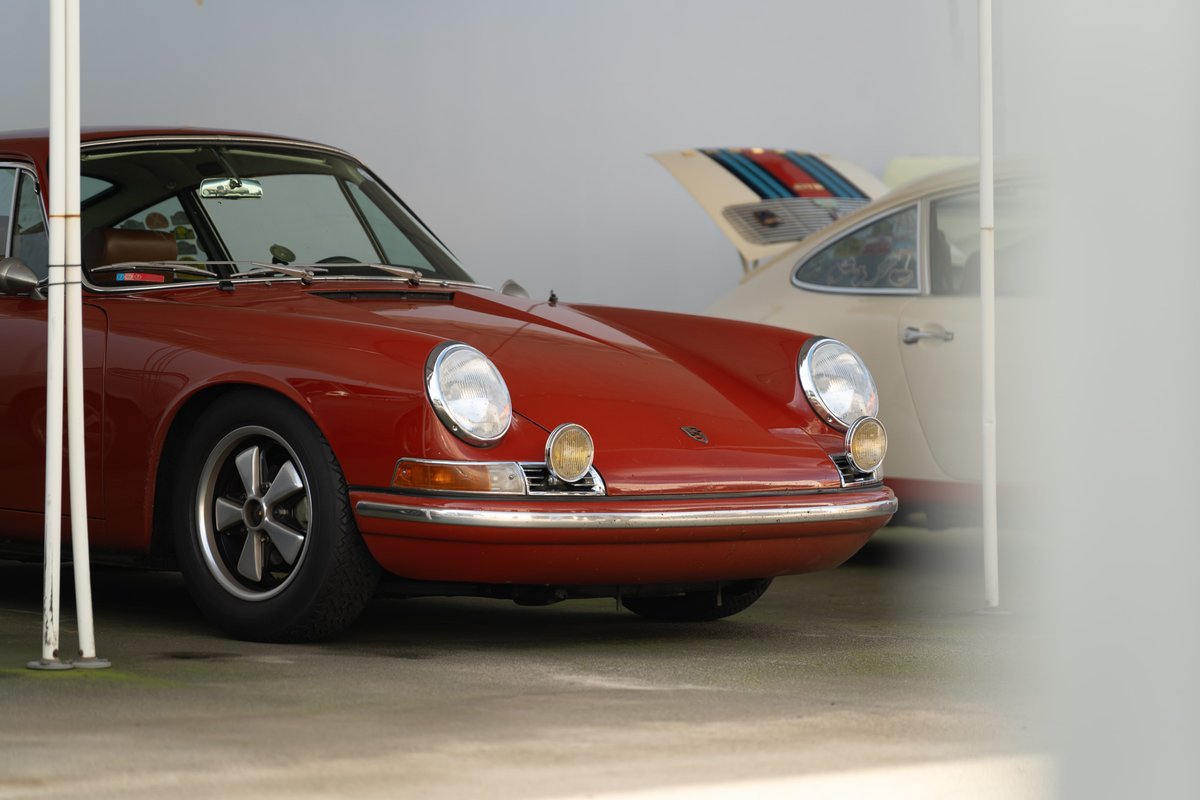Red 1970s Porsche 911 with Fuchs wheels parked next to a Martini livery car.