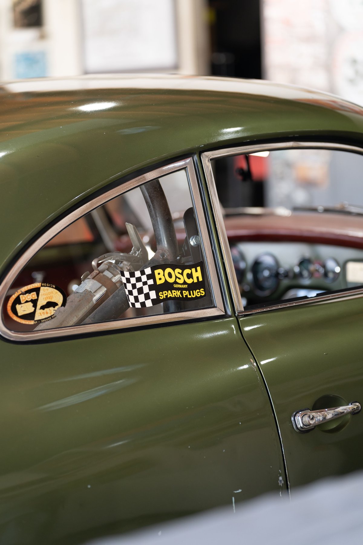 Close-up of a green 1965 Porsche 356SC coupe door with a Bosch Spark Plugs sticker on the window.