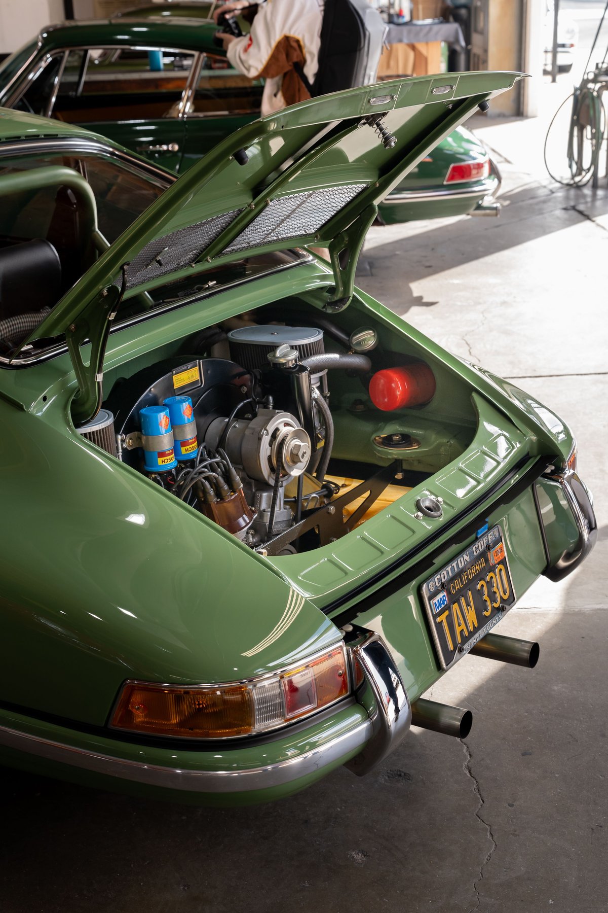 Green 1973 Porsche 911 Targa engine bay open, revealing air-cooled flat-six engine.