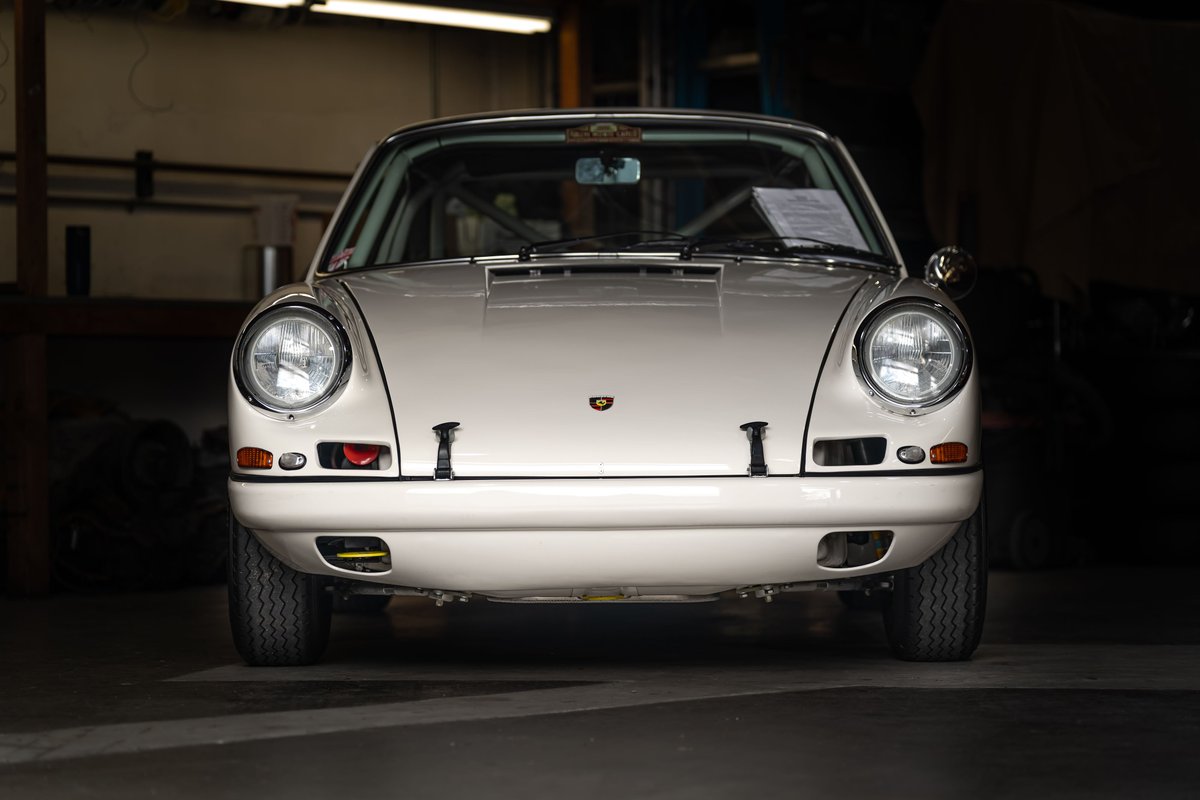 Front view of a vintage white Porsche 911 race car with black rims and roll cage visible.