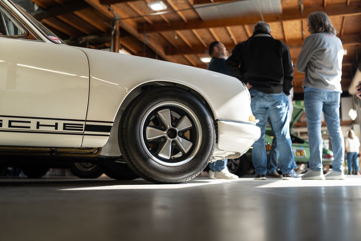 Close-up of a white Porsche 911 side trim and Fuchs wheels at a car show.