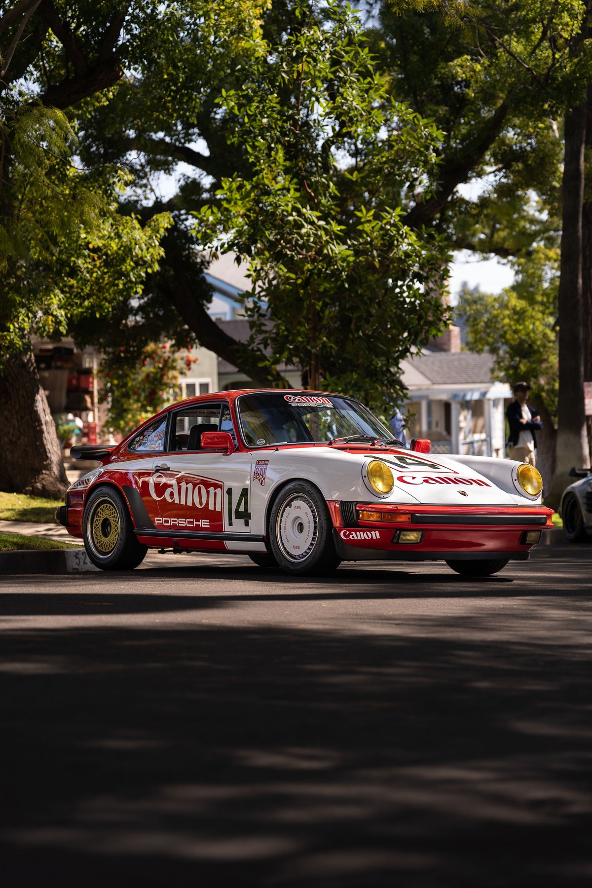 Canon-liveried Porsche 911 Carrera, featuring gold and white rims, red trim, and yellow headlights.
