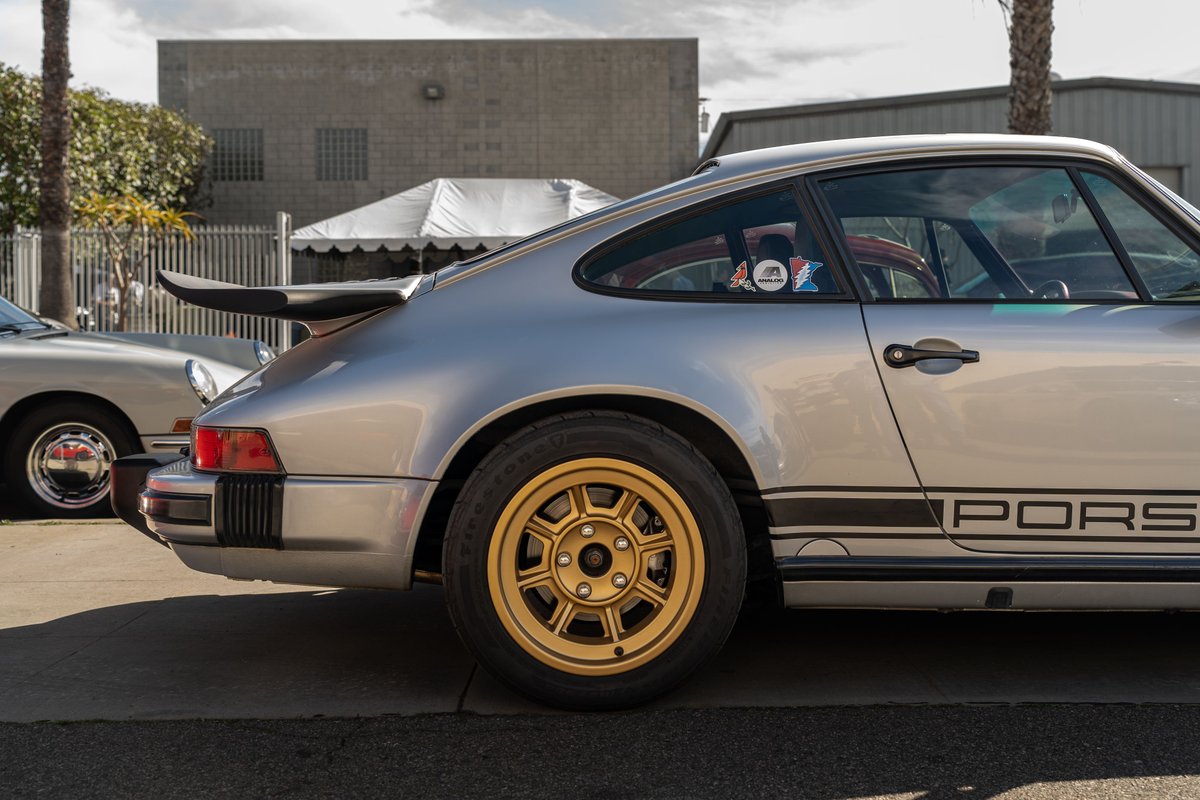 Silver Porsche 911 with gold Fuchs rims and black livery.